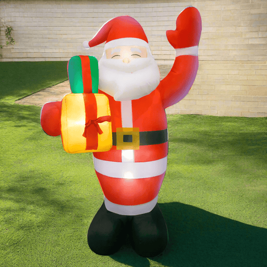 Inflatable Santa Claus holding gifts in front of a decorated house with Christmas lights.