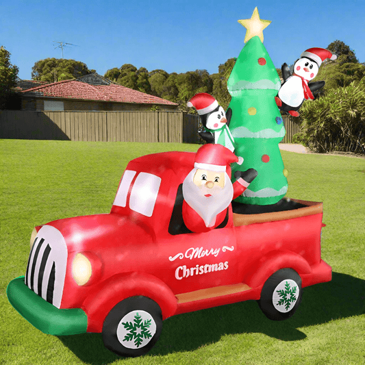Inflatable Christmas scene with red truck, Santa, Christmas tree, and penguins on a white background