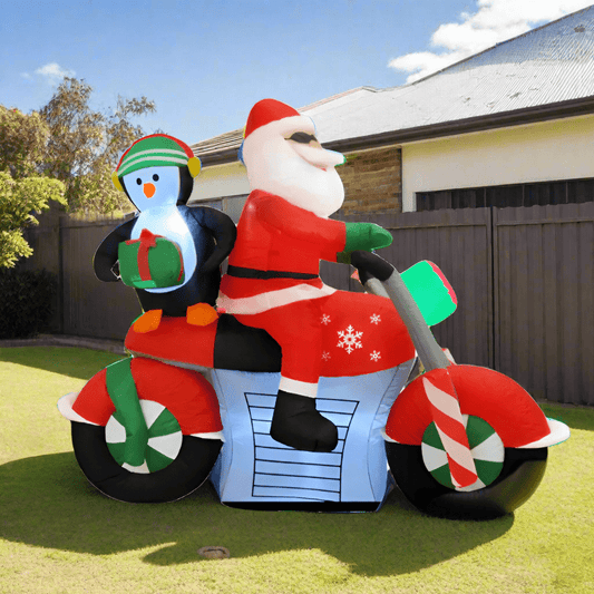 Inflatable Santa Claus riding a motorcycle with a penguin holding a gift on a white background